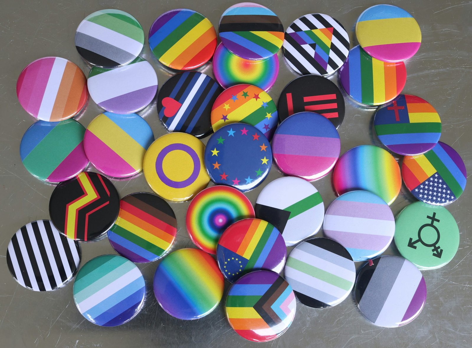 a pile of colorful buttons with various lgbtqia+ flag patterns sitting on top of a table